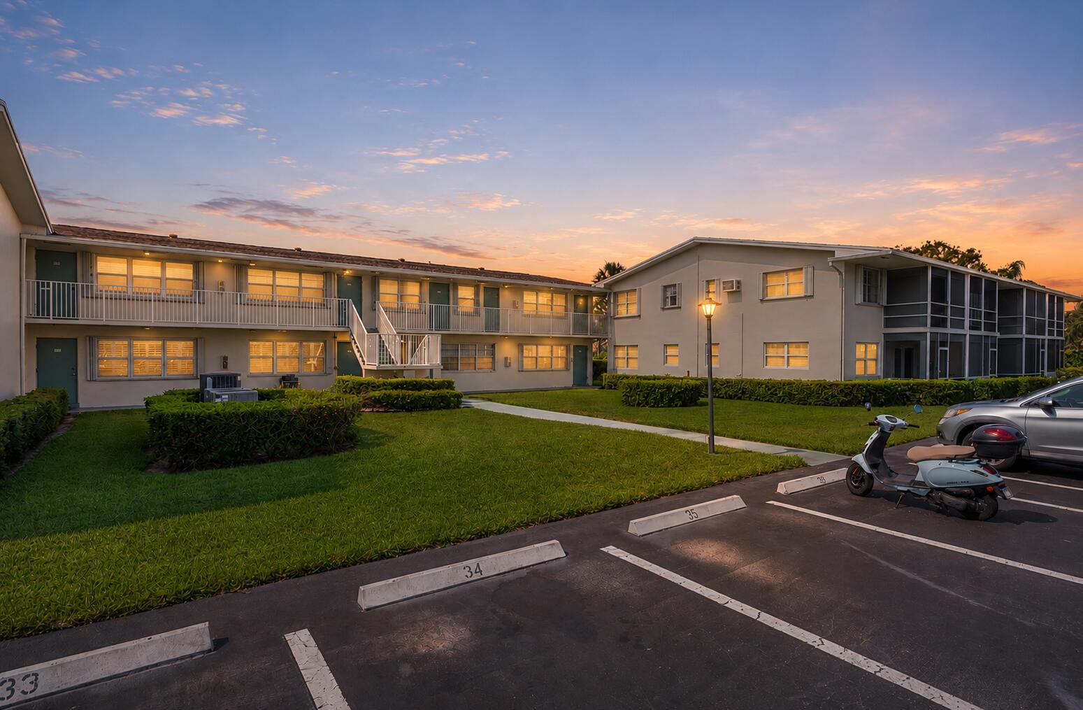 Exterior view of two-story apartment buildings with parking spaces and a scooter at sunset — 740 W Horizons W # 203, Boynton Beach FL 33435, BOYNTON BEACH, FL