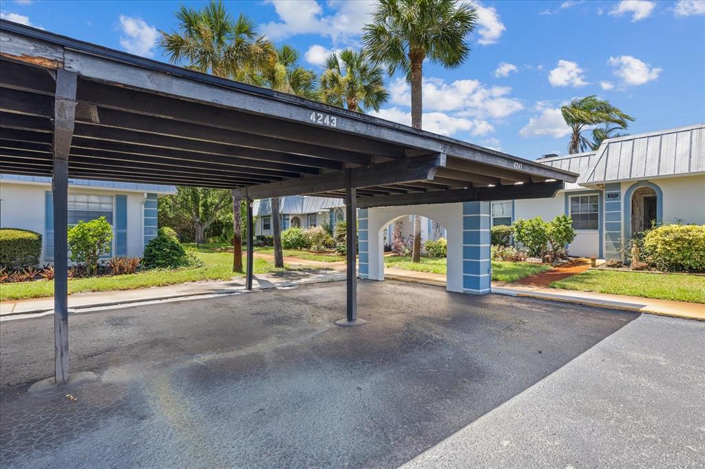 A covered carport structure stands in front of residential buildings with palm trees and landscaping — 4243 RICHMERE DRIVE UNIT 3B, NEW PORT RICHEY, FL