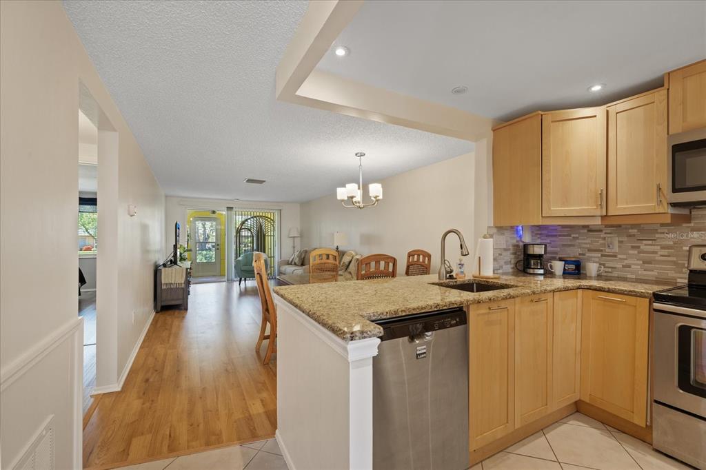 A kitchen with light wood cabinets and granite countertops overlooks a living and dining area — 4243 RICHMERE DRIVE UNIT 3B, NEW PORT RICHEY, FL