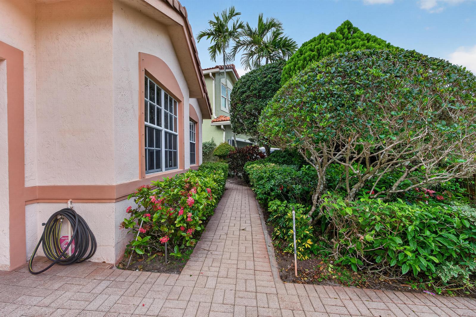 A paved walkway leads between a stucco house wall and dense landscaping toward a neighboring home — 4889 N Classical Boulevard, Delray Beach FL 33445, DELRAY BEACH, FL