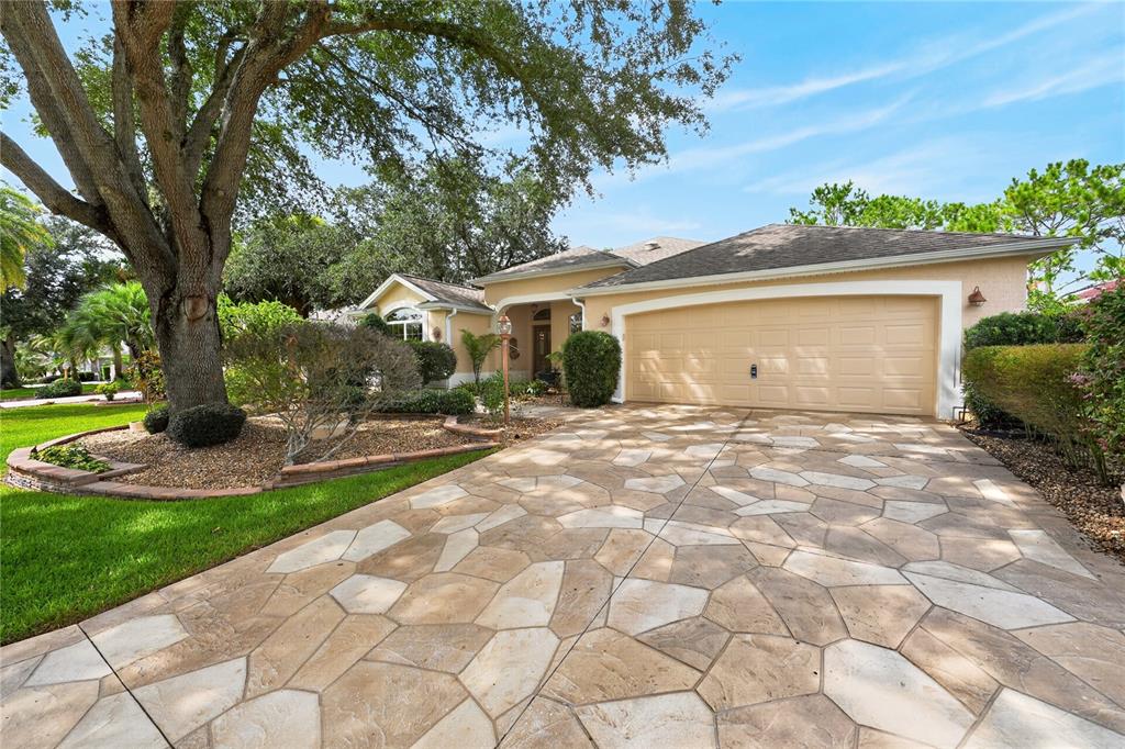 A single-story house with a tan stucco exterior, a large garage, and a stone-patterned driveway — 8901 SE 177TH GRASSMERE STREET, THE VILLAGES, FL