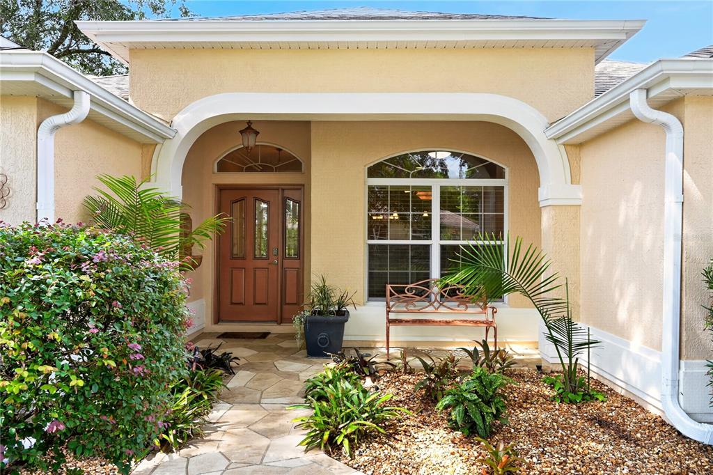 The front entrance of a house features a stone walkway, a brown door, and landscaping — 8901 SE 177TH GRASSMERE STREET, THE VILLAGES, FL