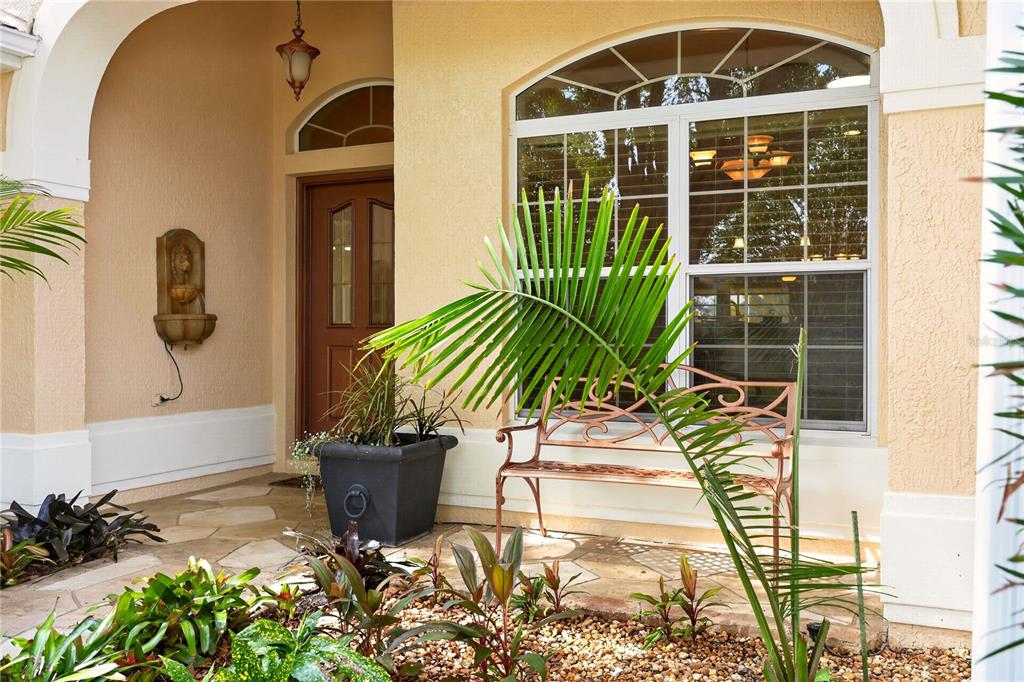 A front porch features a metal bench, a potted plant, and a wall-mounted fountain — 8901 SE 177TH GRASSMERE STREET, THE VILLAGES, FL