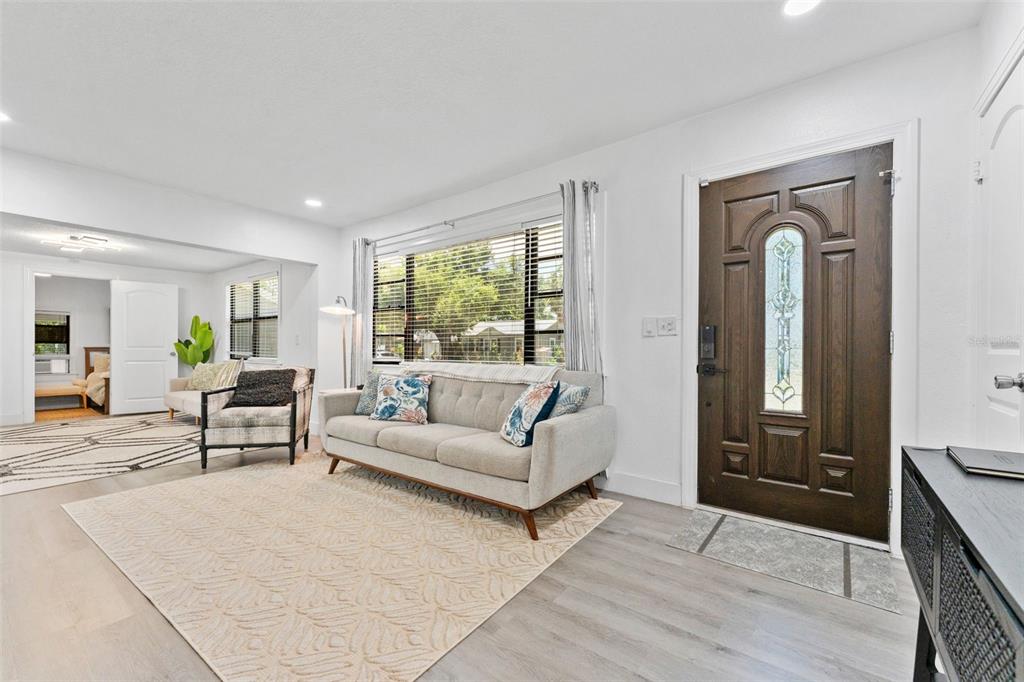 A living room features light wood-look flooring, a gray sofa, and a dark wood front door — 3709 W GRIFLOW STREET, TAMPA, FL