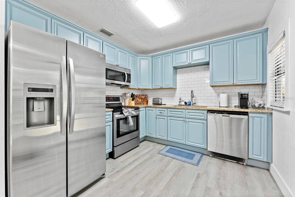 A kitchen features light blue cabinets, stainless steel appliances, granite countertops, and a white backsplash — 3709 W GRIFLOW STREET, TAMPA, FL