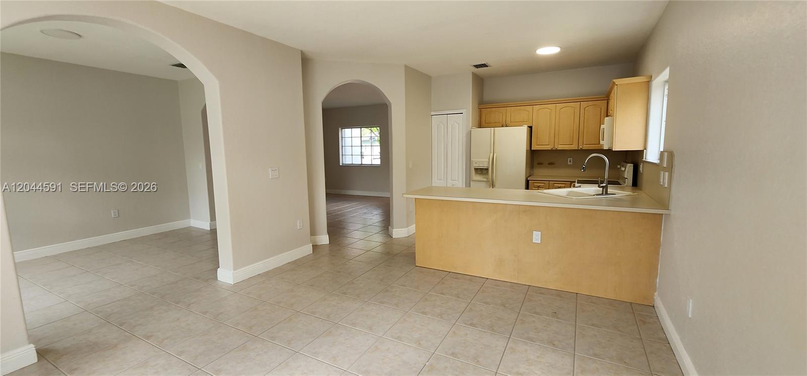 An open-concept kitchen with light wood cabinets and a breakfast bar overlooks a tiled room — 16507 NW 91st Ave, Miami Lakes FL 33018, MIAMI LAKES, FL