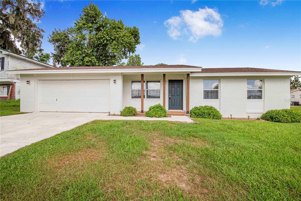 A single-story white brick house with a two-car garage and a dark front door — 4921 SHARON AVENUE, LAKELAND, FL