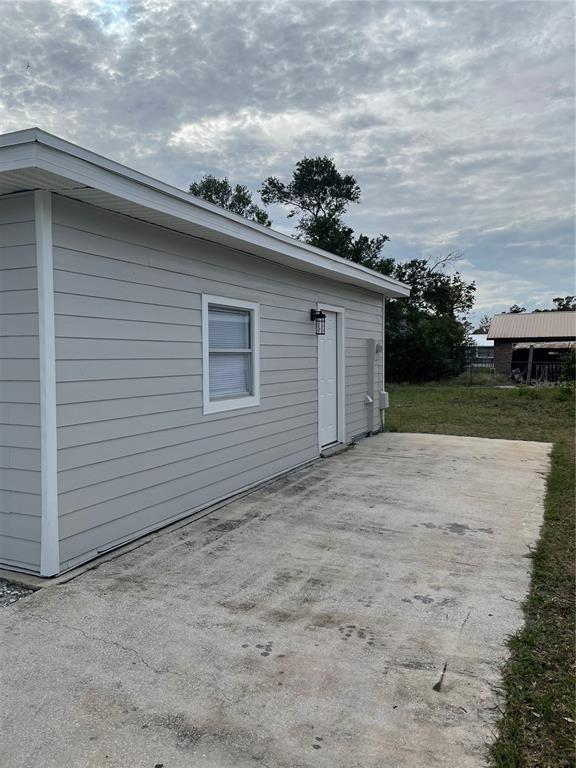 A light gray exterior wall with a window, a door, and a concrete patio — 603 MAGGIE CIRCLE, WINTER HAVEN, FL
