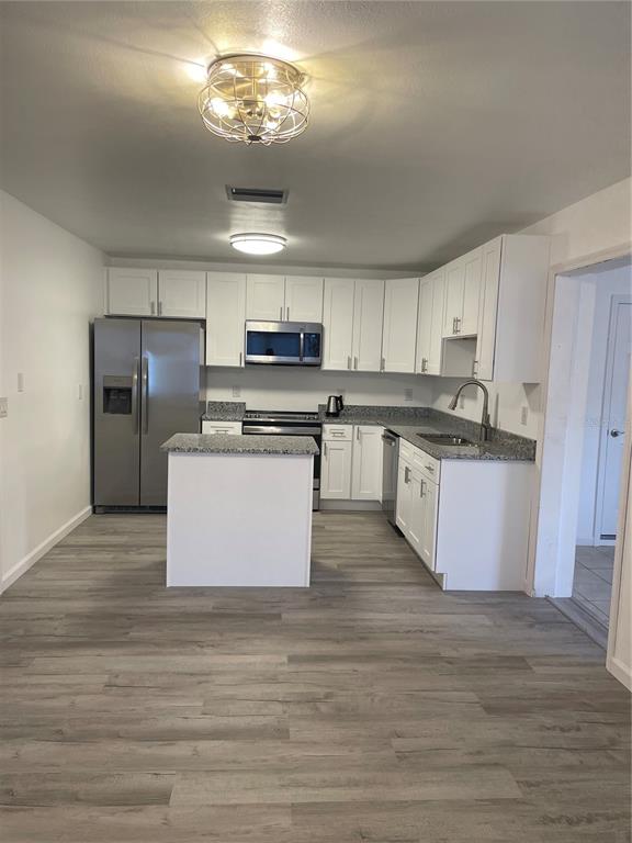 A kitchen features white cabinets, granite countertops, stainless steel appliances, and gray wood-look flooring — 603 MAGGIE CIRCLE, WINTER HAVEN, FL