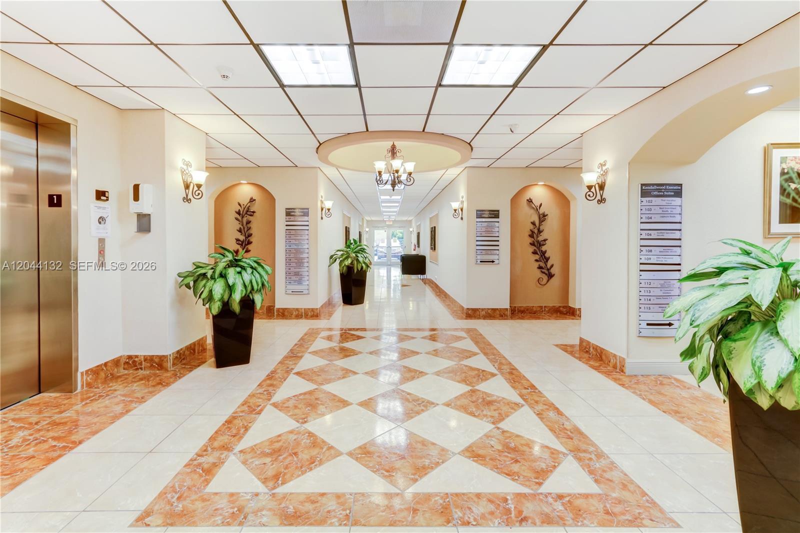 A brightly lit office building lobby features a tiled floor, potted plants, and elevator access — 12150 SW 128th Ct # 138, Miami FL 33186, MIAMI, FL