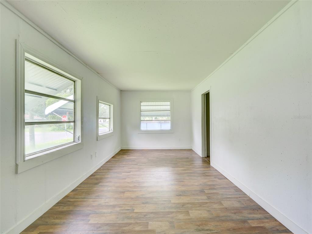 An empty room features white walls, wood-look flooring, and three windows — 813 NW 5TH STREET, WEBSTER, FL
