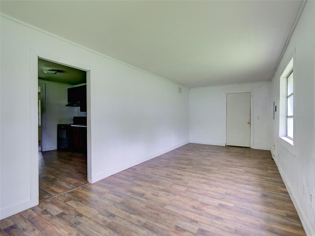 An empty room with white walls, wood-look flooring, and a doorway leading to a kitchen — 813 NW 5TH STREET, WEBSTER, FL