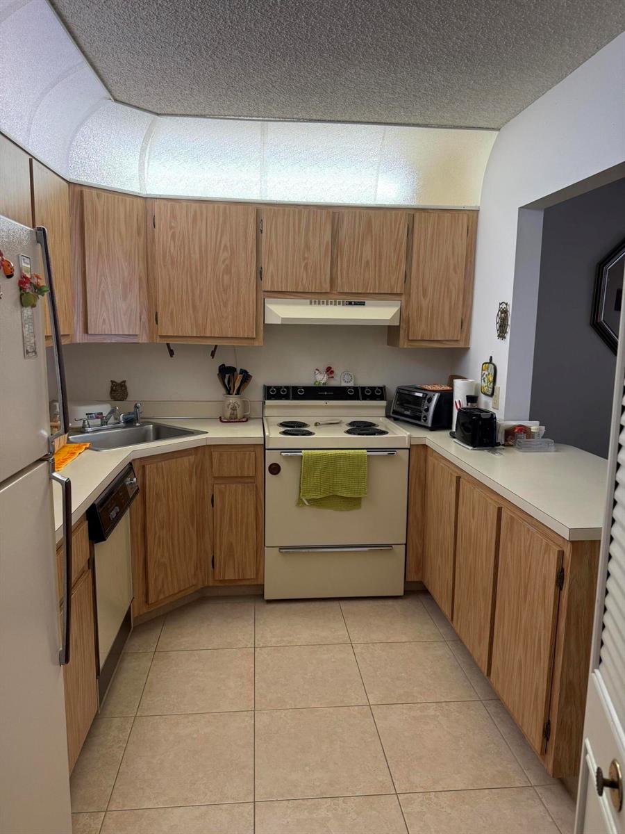 A kitchen features light wood cabinets, white appliances, a corner sink, and beige tile flooring — 422 Pine Glen Lane # 1, FL 33463, FL