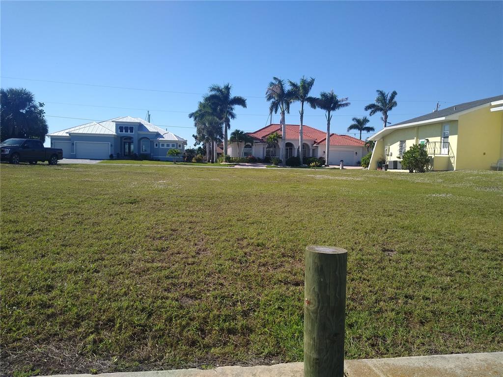 A vacant grassy lot sits in front of several houses and palm trees under a clear sky — 116 COLONIAL STREET SE, PORT CHARLOTTE, FL