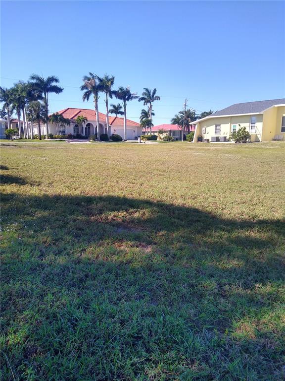 A vacant grassy lot sits in front of several suburban houses with palm trees — 116 COLONIAL STREET SE, PORT CHARLOTTE, FL
