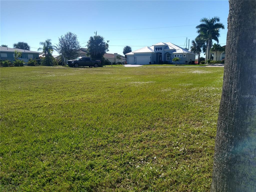 A large, grassy vacant lot sits in front of a blue house and a pickup truck — 116 COLONIAL STREET SE, PORT CHARLOTTE, FL