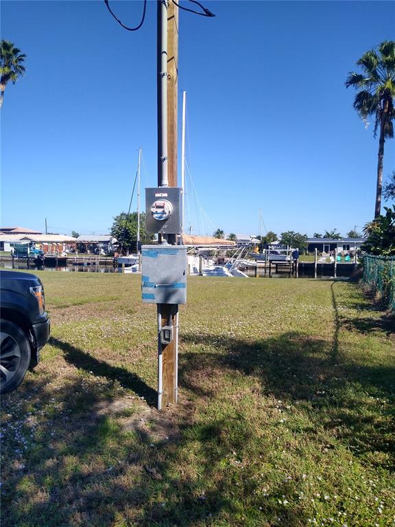 A utility pole with an electrical meter and service box stands on a grassy waterfront lot — 116 COLONIAL STREET SE, PORT CHARLOTTE, FL