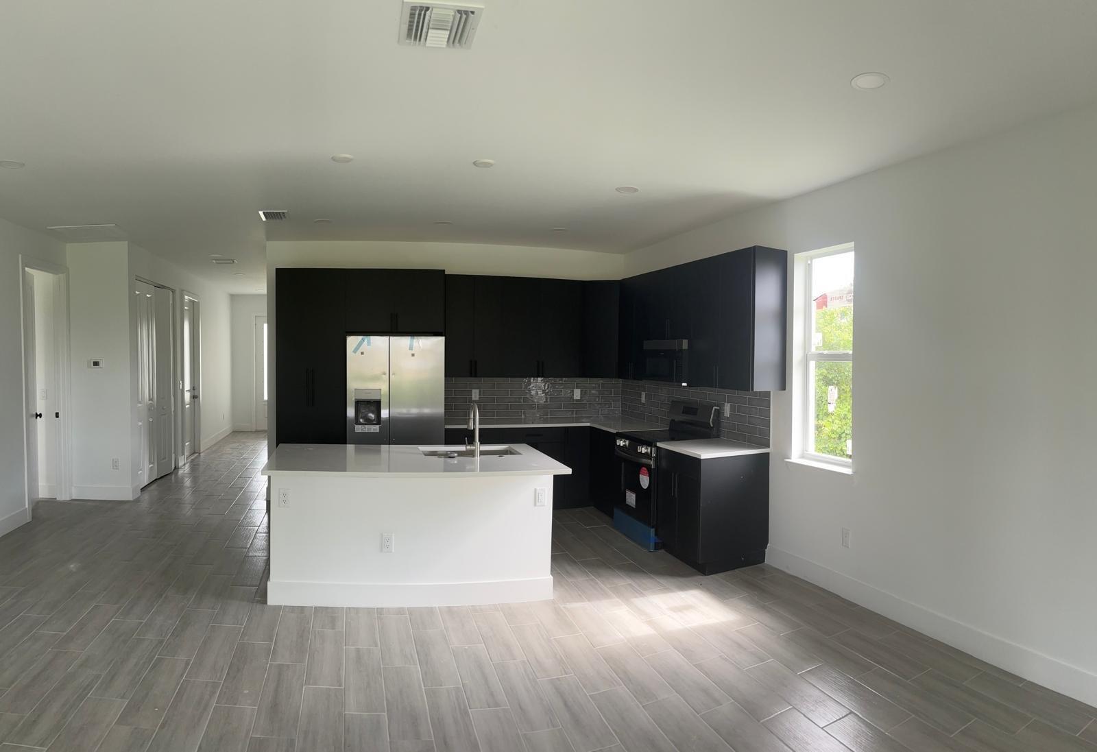 A modern kitchen features black cabinets, a white island, stainless steel appliances, and gray flooring — 136 Lomas Rd Road, FL 33947, FL