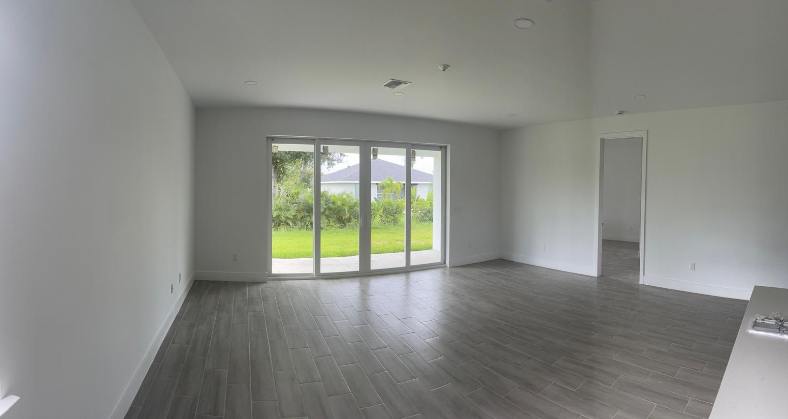 An empty living room with gray tile flooring, white walls, and a sliding glass door — 136 Lomas Rd Road, FL 33947, FL