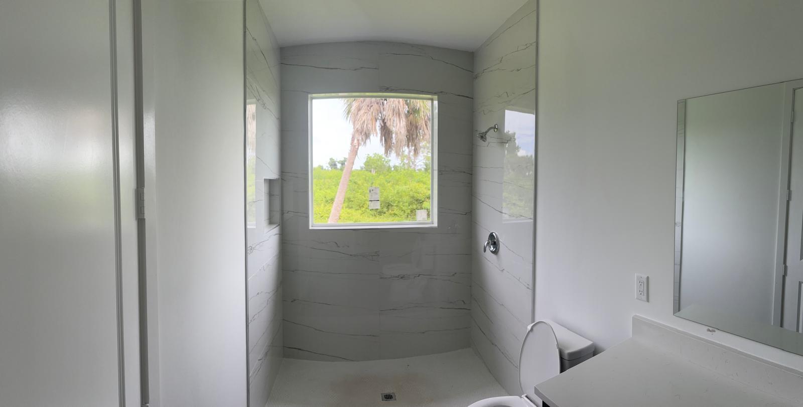 A bathroom featuring a walk-in shower with marble-look tile, a window, and a vanity mirror — 136 Lomas Rd Road, FL 33947, FL