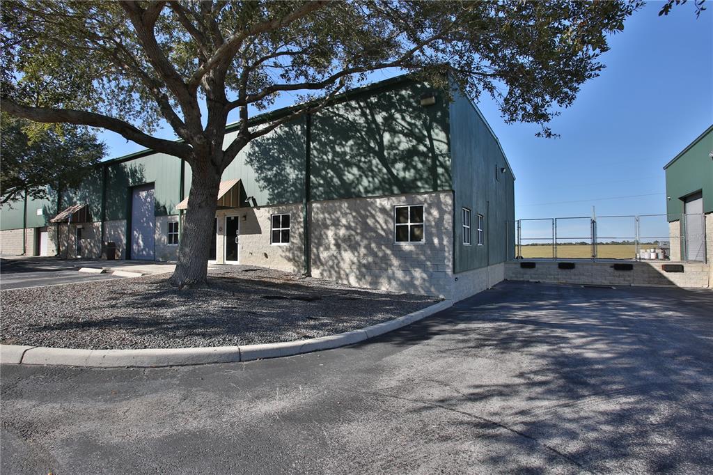An exterior view of a commercial warehouse building with a paved parking lot and tree — 7731 SE 59TH COURT UNIT 300, OCALA, FL