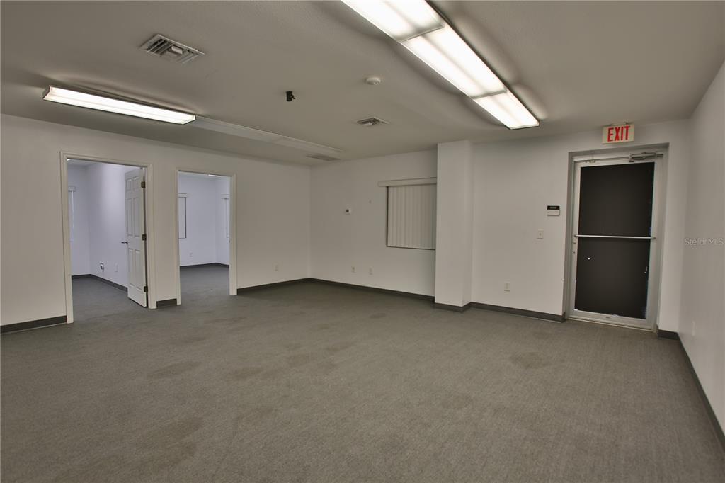 An empty office space features gray carpeting, white walls, fluorescent lighting, and an exit door — 7731 SE 59TH COURT UNIT 300, OCALA, FL