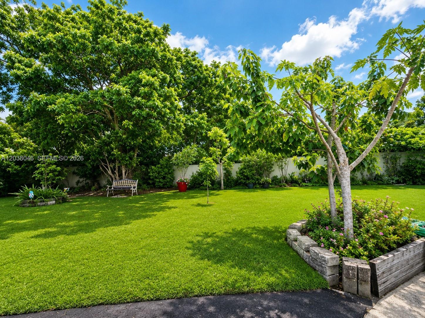 A lush green backyard features a large tree, a stone-bordered garden bed, and a bench — 13870 Magnolia Ct, Davie FL 33325, DAVIE, FL