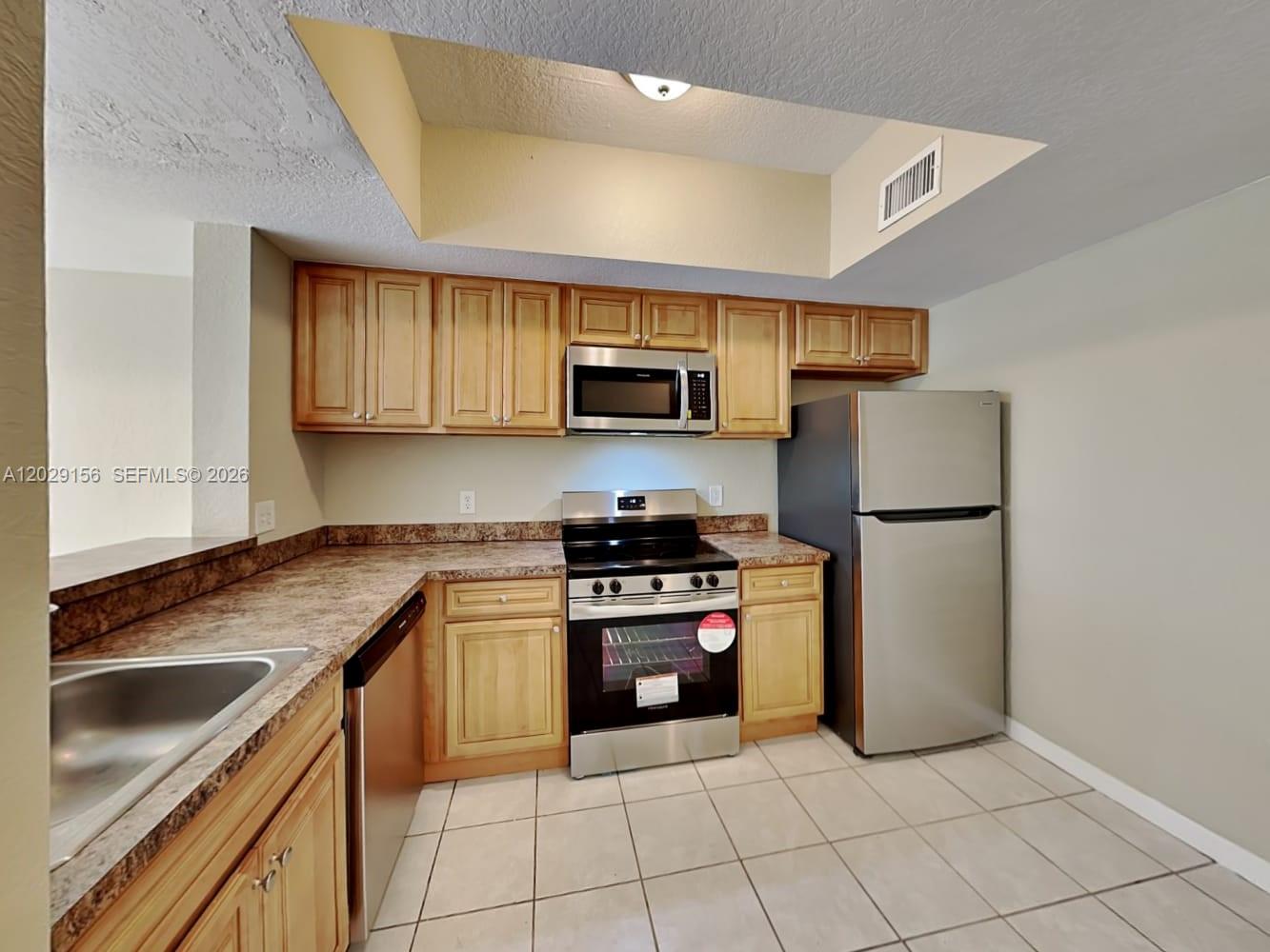 A kitchen features light wood cabinets, stainless steel appliances, and beige tile flooring — SUNRISE, FL