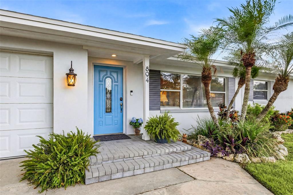 The exterior of a house features a bright blue front door and a brick porch — 894 JOAN STREET, DUNEDIN, FL