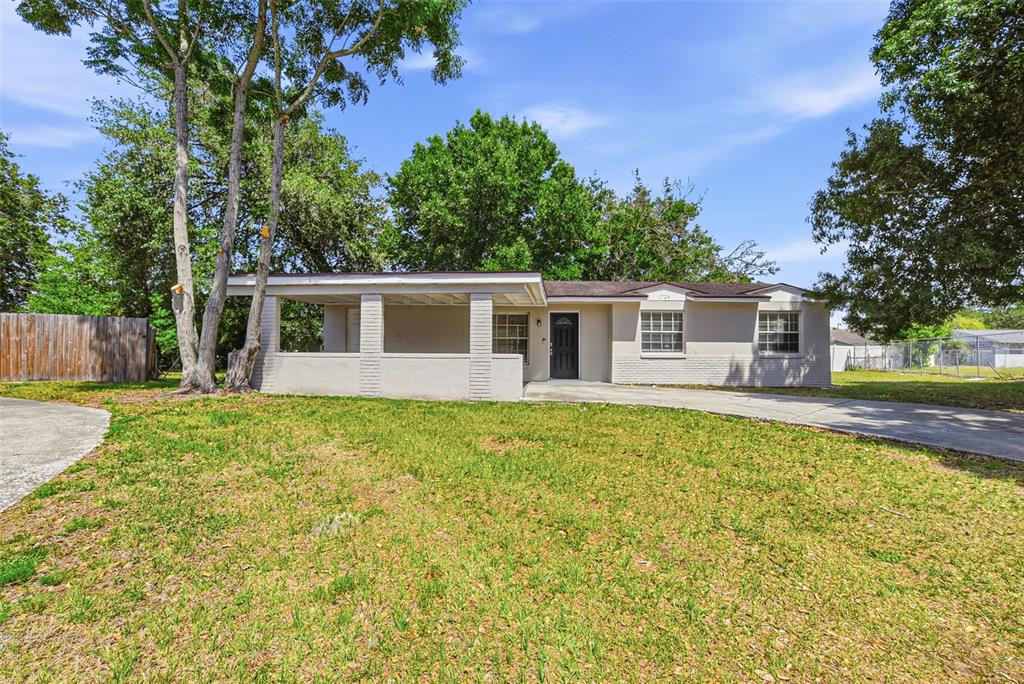 A single-story house with a covered front porch, a concrete driveway, and surrounding mature trees — 1729 FLORES COURT, ORLANDO, FL