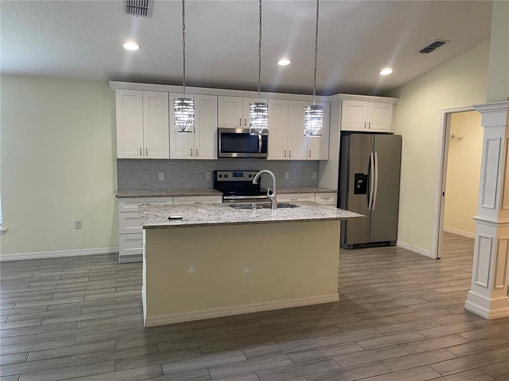 A kitchen features white cabinets, granite countertops, a central island, and stainless steel appliances — 208 MISSOURI AVENUE, ST CLOUD, FL