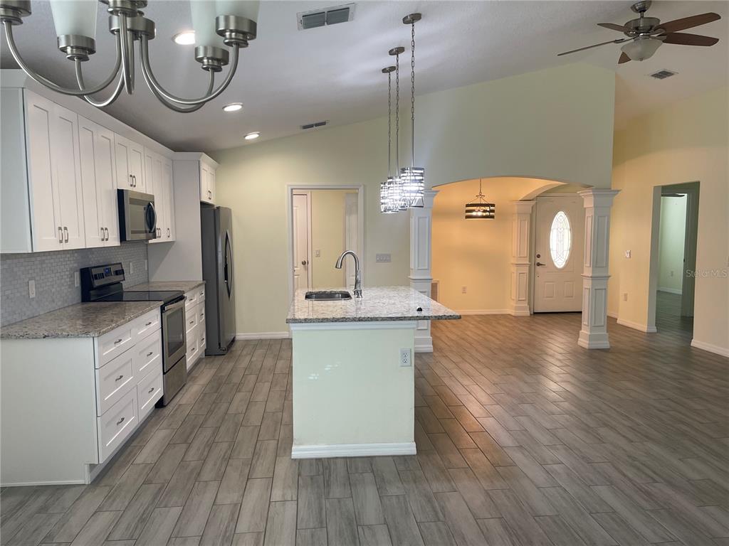 A kitchen with white cabinets, granite countertops, and an island overlooks an entryway with columns — 208 MISSOURI AVENUE, ST CLOUD, FL