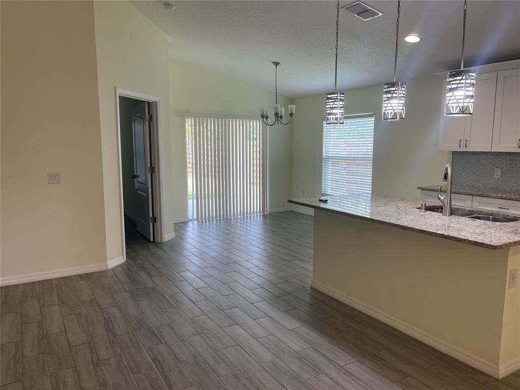 A kitchen with granite countertops and pendant lights overlooks a dining area with tile floors — 208 MISSOURI AVENUE, ST CLOUD, FL