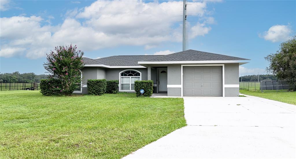 A single-story gray house with a garage and a large lawn under a cloudy sky — 604 BOITNOTT LANE, BUSHNELL, FL
