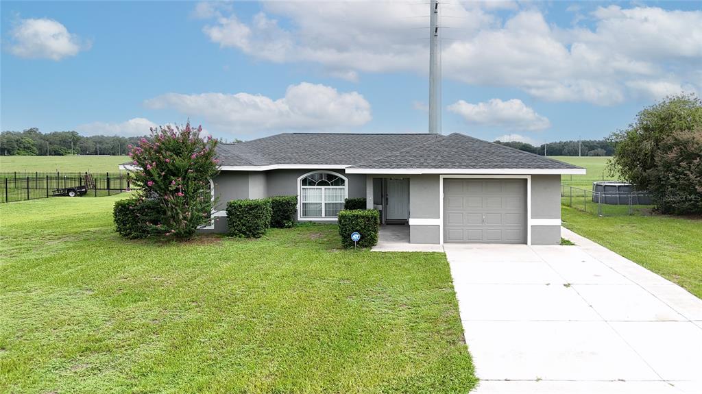 A single-story gray house with a garage, arched window, and a large grassy yard — 604 BOITNOTT LANE, BUSHNELL, FL