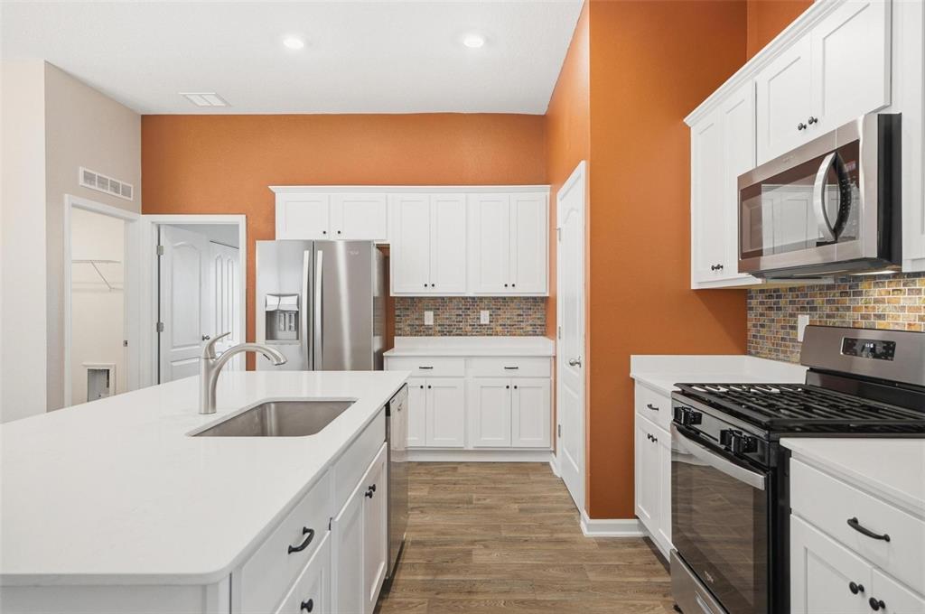 A kitchen features white cabinets, stainless steel appliances, a center island, and orange walls — 5 CADDY COURT, BUNNELL, FL