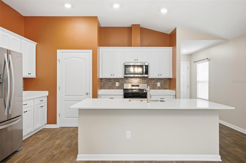 A kitchen features white cabinets, a central island, stainless steel appliances, and orange accent walls — 5 CADDY COURT, BUNNELL, FL