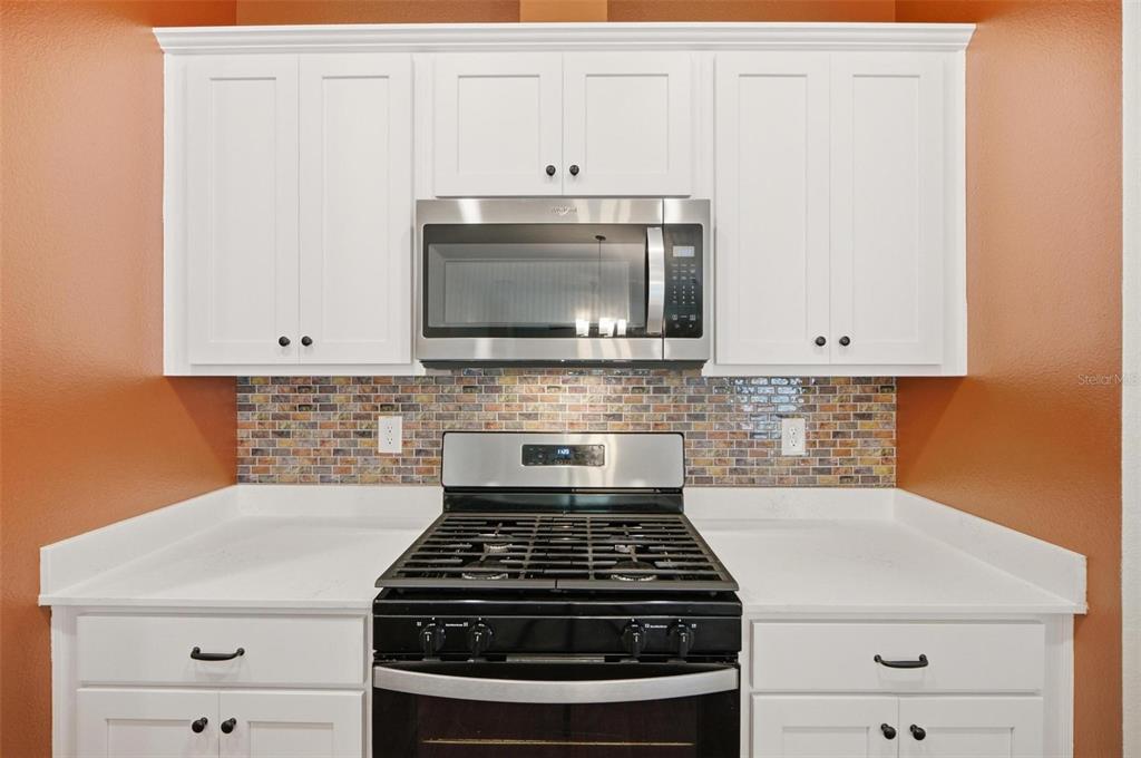 A kitchen features white cabinets, a stainless steel microwave, a gas range, and mosaic backsplash — 5 CADDY COURT, BUNNELL, FL