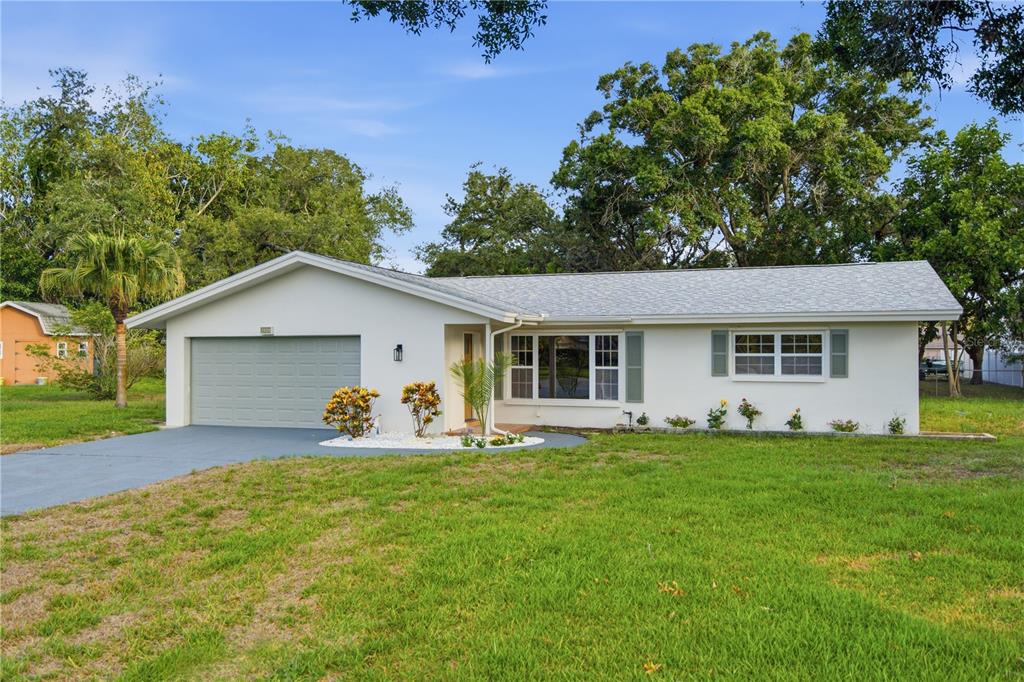 A single-story house with a white exterior, gray garage door, and a large front lawn — 1920 CANADIANA COURT, DUNEDIN, FL