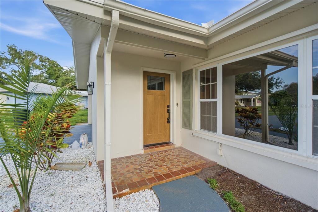 A front entryway features a wooden door, tiled porch, and a large window with shutters — 1920 CANADIANA COURT, DUNEDIN, FL