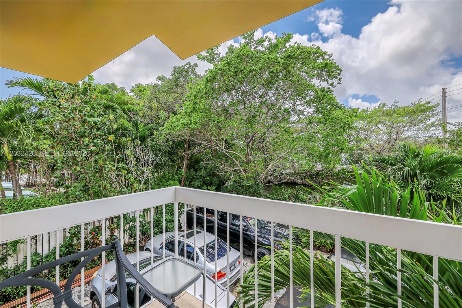 A balcony view overlooks a parking area, lush green trees, and a small canal — 12085 W Dixie Highway, Biscayne Park FL 33161, BISCAYNE PARK, FL