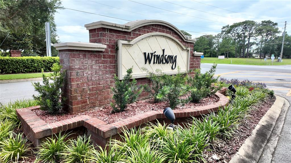 A brick monument sign for Windsong sits in a landscaped garden bed near a road — 5620 WINDSONG OAK DRIVE, LEESBURG, FL