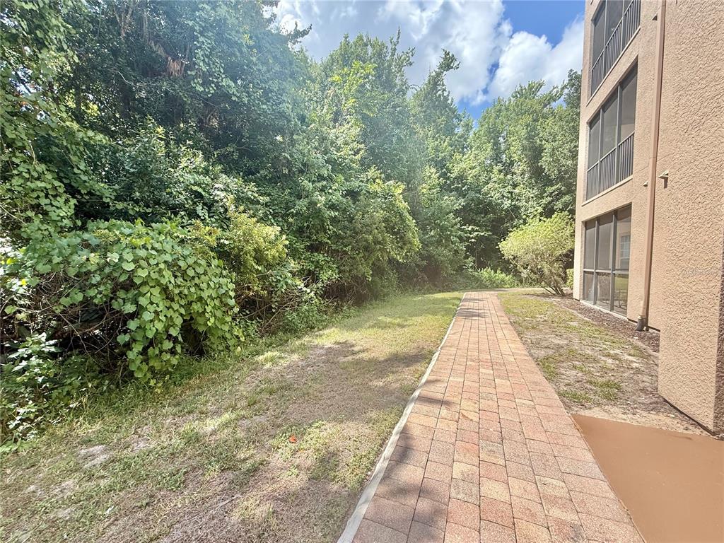 A brick walkway runs alongside a multi-story building next to a dense wooded area — 1301 TUSCAN TERRACE UNIT 9106, DAVENPORT, FL