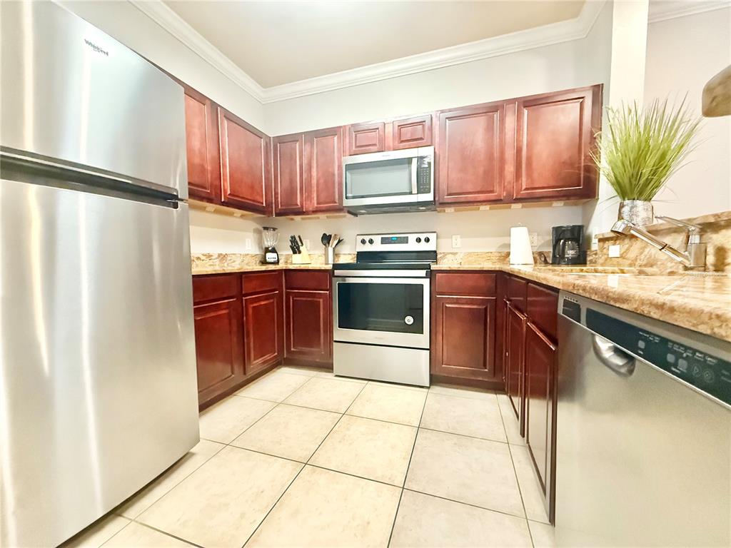 A kitchen features stainless steel appliances, dark wood cabinets, and beige tile flooring — 1301 TUSCAN TERRACE UNIT 9106, DAVENPORT, FL