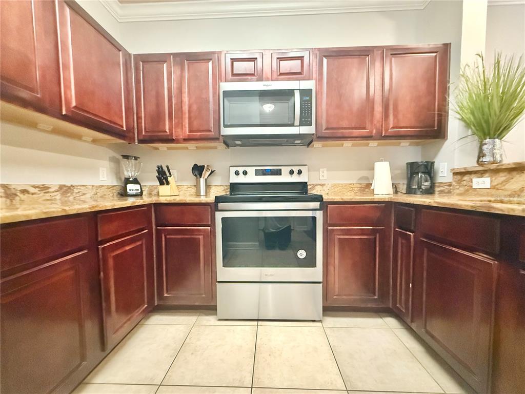A kitchen features dark wood cabinets, stainless steel appliances, and tan granite countertops — 1301 TUSCAN TERRACE UNIT 9106, DAVENPORT, FL