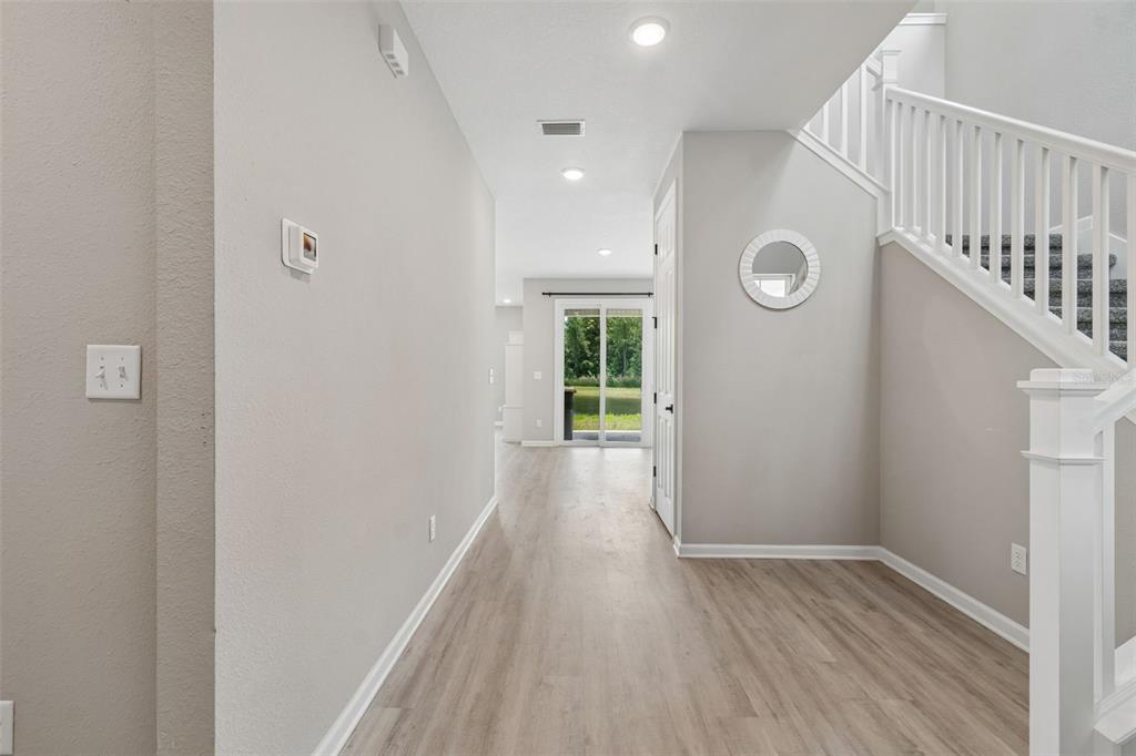 A hallway with light wood-look flooring leads to a sliding glass door with outdoor views — 8268 MARIETTA STILL DRIVE, JACKSONVILLE, FL