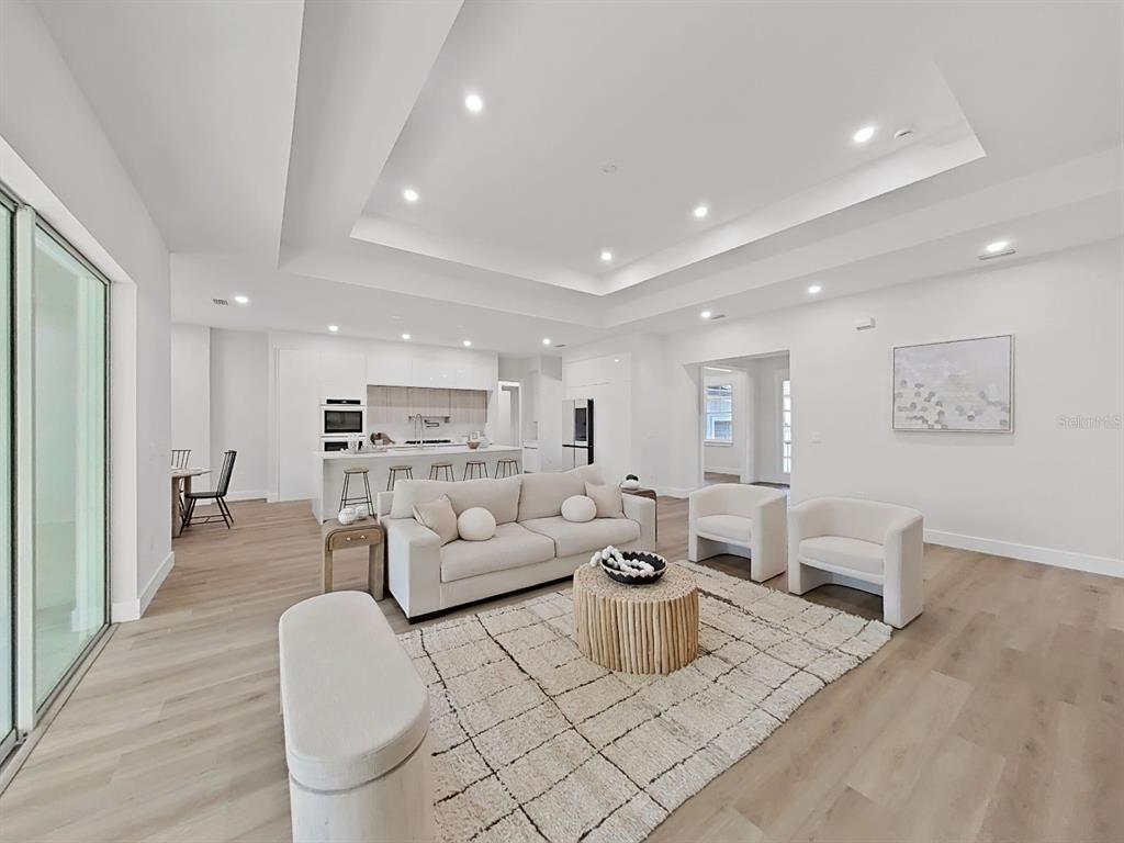 A modern open-concept living room features a white sofa, two armchairs, and light wood flooring — 4507 MAJESTIC HILL LOOP, BROOKSVILLE, FL