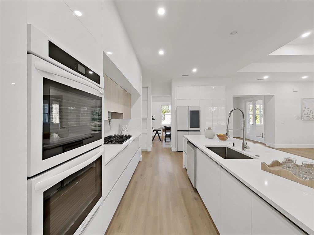 A modern white kitchen features a large island, stainless steel appliances, and light wood flooring — 4507 MAJESTIC HILL LOOP, BROOKSVILLE, FL