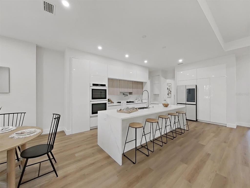 A modern kitchen features white cabinetry, a marble-topped island with bar stools, and wood flooring — 4507 MAJESTIC HILL LOOP, BROOKSVILLE, FL