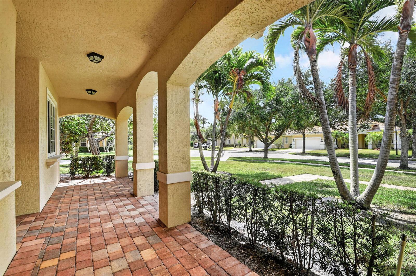 A covered porch with brick pavers and arched columns overlooks a grassy suburban street — 6810 Osage Circle, FL 33413, FL